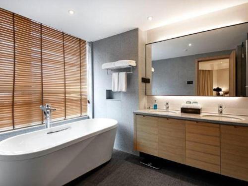 a bathroom with a large tub and a large mirror at New Century Kylie Hotel Ningbo in Ningbo