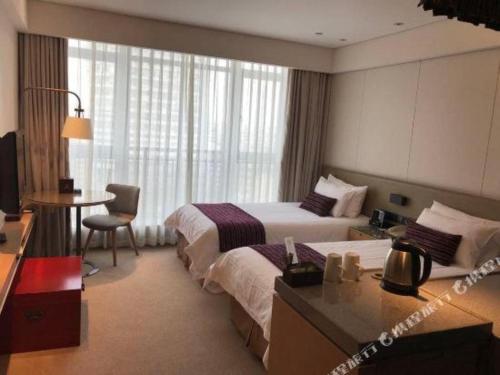 a hotel room with two beds and a desk at New Century Kylie Hotel Ningbo in Ningbo