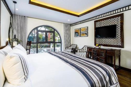 a bedroom with a white bed and a television at Le Pavillon Hoi An Paradise Hotel & Spa in Hoi An