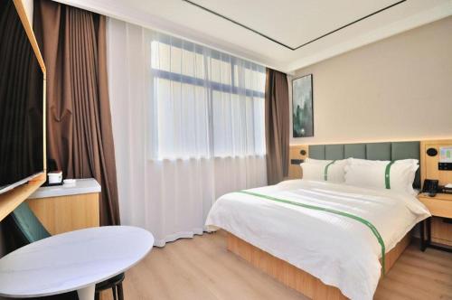 a hotel room with a large bed and a table at GreenTree Inn Suzhou Shihu Suli Road Express Hotel in Suzhou