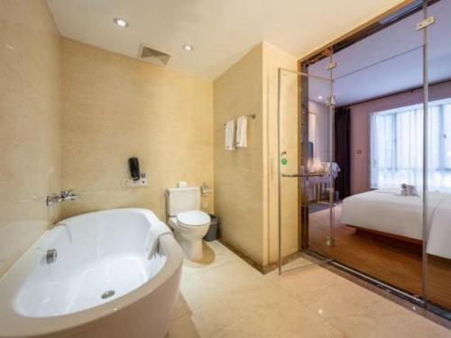 a bathroom with a tub and a toilet and a bed at Expo Garden Hotel in Kunming
