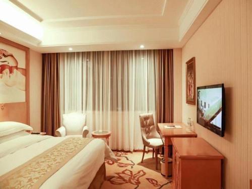 a hotel room with a bed and a desk and a television at Vienna Classic Hotel Qingdao Huangdao in Huangdao