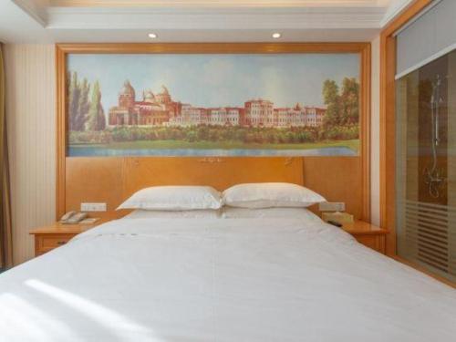 a bedroom with a large bed with a painting on the wall at Vienna Classic Hotel Qingdao Huangdao in Huangdao