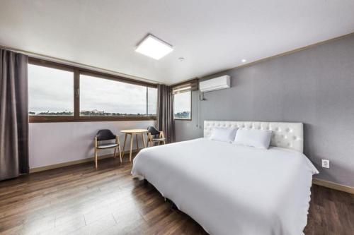 a bedroom with a large white bed and a table at Orange Hotel Jeju in Seogwipo