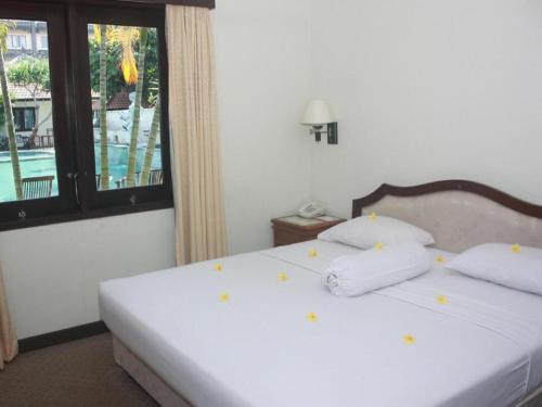 a bedroom with a white bed with pillows and a window at Jimbarwana Hotel in Negara