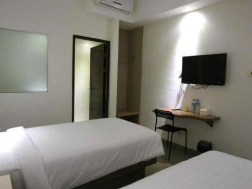a bedroom with two beds and a desk with a television at Hart Hotel Arjuna in Gili Trawangan