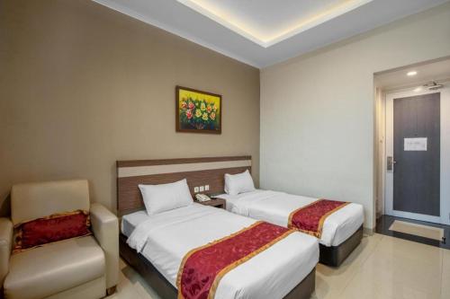 a hotel room with two beds and a chair at Raffleshom Hotel in Bandung
