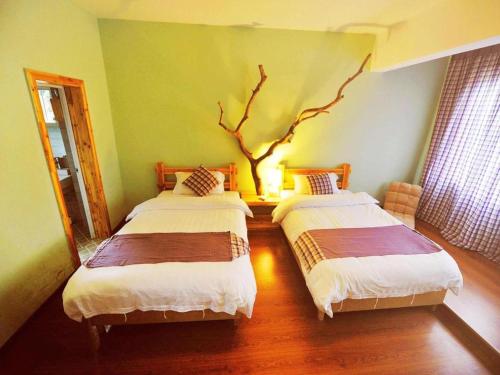 two beds in a room with a tree on the wall at Spring Flowers Blossoming Hotel in Yangshuo
