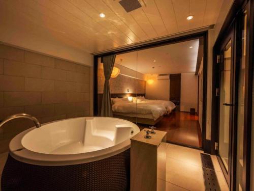 a bathroom with a tub and a bedroom with a bed at Kannawa Onsen Hotel Sansuikan in Beppu
