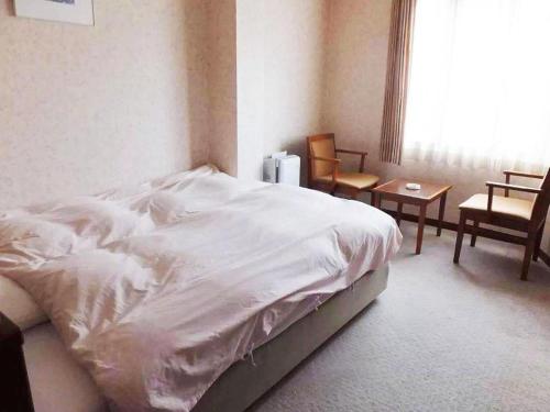 a bedroom with a white bed and chairs and a window at Sento Otani Hotel in Toyooka