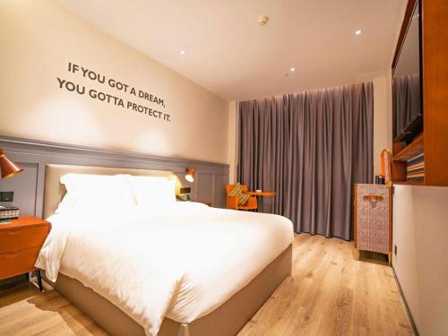 a bedroom with a bed with a sign on the wall at City Comfort Premier Hotel Xiaogan Anlu Railway Station Dongda Times Square in Xiaogan