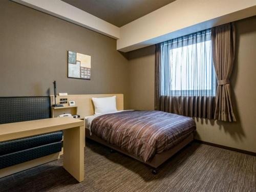 a hotel room with a bed and a desk and a window at Hotel Route Inn Grand Kitami Ekimae in Kitami