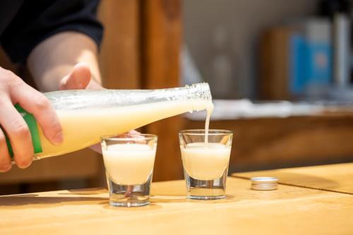 a person pouring a bottle of milk into two glasses at 長浜城下 町屋ホテル 和乃リトリートひといき in Nagahama