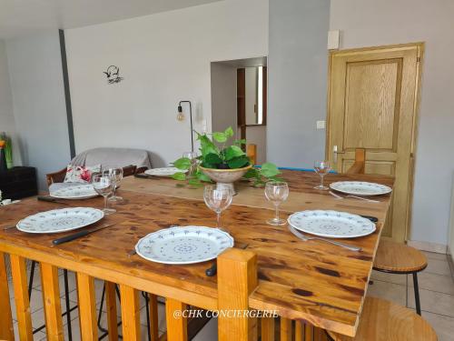 une table en bois avec des assiettes et des verres à vin dessus dans l'établissement Le Repère Charmant Appartement Familial au Cœur des Herbiers à 12 min du Puy duFou, aux Herbiers