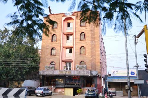 a tall brick building with cars parked in front of it at Sakthi Hotel in Pollāchi