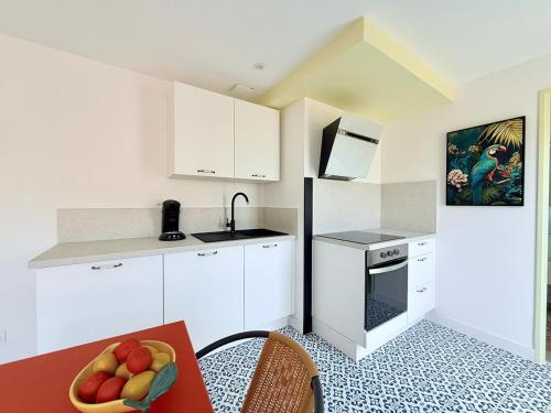 - une cuisine avec des placards blancs et une table avec un bol de fruits dans l'établissement L'Entre-Rives, à Rochefort