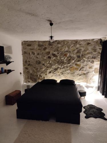a bedroom with a black bed and a stone wall at Artemis Studio Pyrgi no1 in Platis Gialos