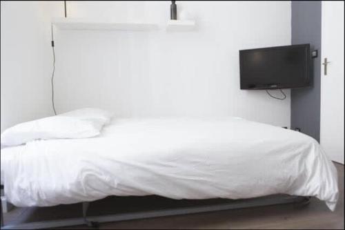 - une chambre avec un lit blanc et une télévision murale dans l'établissement Studio hyper centre historique Quai bourgeois, à Bordeaux