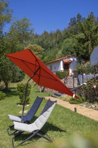 two chairs and a red umbrella in the grass at Magnolias Cottage in Lousã