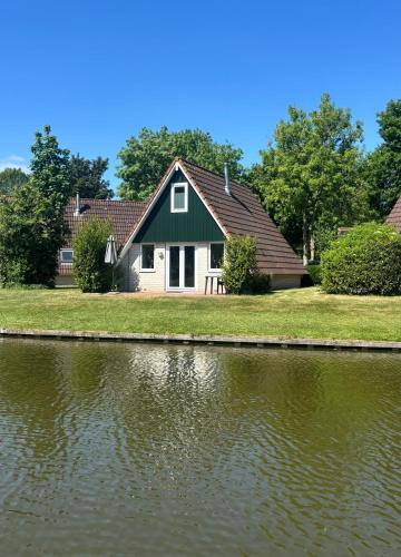 a green and white house next to a body of water at Vakantiewoning Meerrust in Gramsbergen