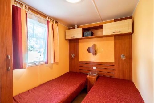 Cette petite chambre comprend 2 lits rouges et une fenêtre. dans l'établissement Mh 25 Les Genêts Ronce les bains, à La Tremblade