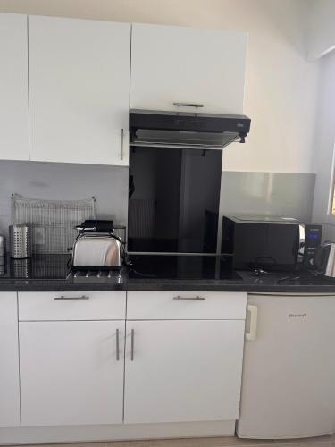 une cuisine avec des armoires blanches et un comptoir noir dans l'établissement Studio lumineux proche de Paris, à Fontenay-aux-Roses