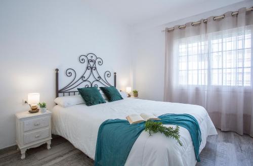 a white bedroom with a large bed and a window at Apartamentos Collado Playa Valdelagrana in El Puerto de Santa María