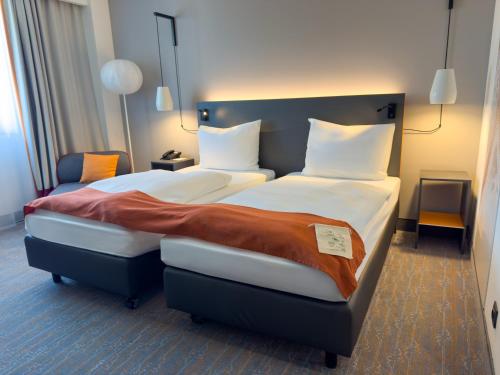 a hotel room with two beds and a chair at Vienna House Easy by Wyndham Bucharest Airport in Otopeni