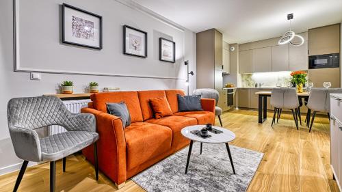 a living room with an orange couch and a kitchen at Źródło Izery przy gondoli VIP Sauna, Siłownia, Bawialnia by Royal Aparts in Świeradów-Zdrój