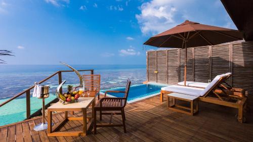 a deck with a table and chairs and an umbrella at Lily Beach Resort and Spa - All Inclusive in Dhangethi