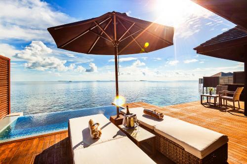 a table with an umbrella on a deck next to the water at Lily Beach Resort and Spa - All Inclusive in Dhangethi