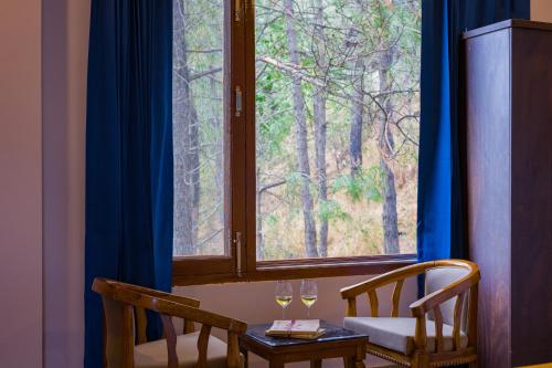 a window with two chairs and two wine glasses on a table at Alaya Stays Archee's 6 BHK Nature Retreat with Game Lounge & Open Dining in Kasauli