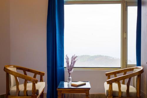 two chairs and a table in front of a window at Alaya Stays Archee's 6 BHK Nature Retreat with Game Lounge & Open Dining in Kasauli