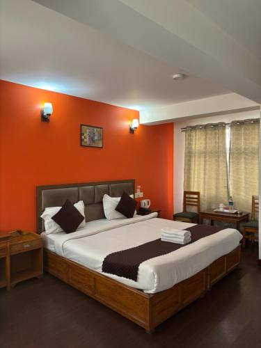 a bedroom with a large bed with an orange wall at Hotel KASTURI PALACE & RESTAURANT DARJEELING in Darjeeling