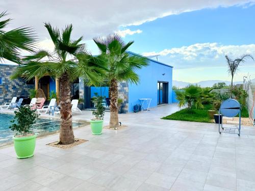 a patio with palm trees and a blue building at Villa Berkane avec Piscine Jacuzzi privée Sans vis-à-vis in Berkawe