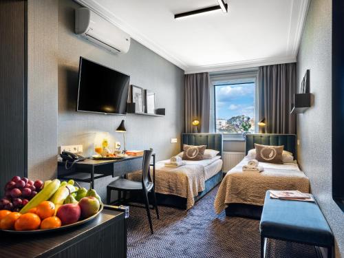 a hotel room with two beds and a table with a bowl of fruit at Hotel Logos Kraków in Krakow