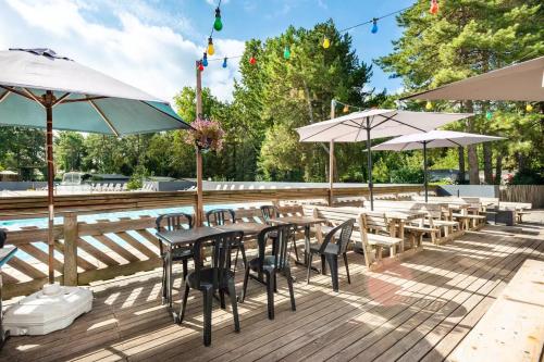 a deck with tables and umbrellas and a pool at Mobil-home climatisé à 5 min de la mer, charmant in Camiers