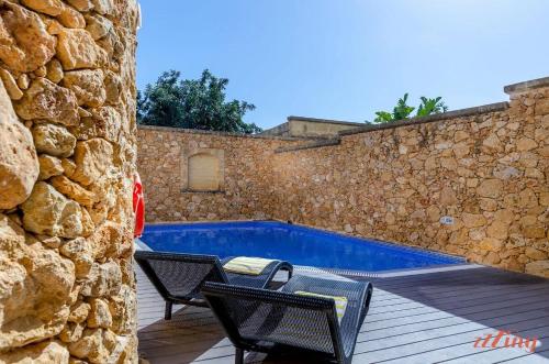 a swimming pool with two chairs and a stone wall at Peaceful Farmhouse Retreat with Pool & Sun Lounger in Xagħra