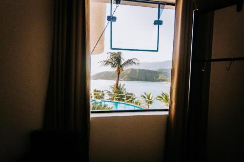 a window with a view of the ocean from a hotel room at Conforto, Vista linda e Pé na Areia | Barequeçaba in São Sebastião