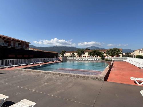 une grande piscine avec des chaises longues et des tables blanches dans l'établissement Idéal familles : T2 climatisé avec terrasse, piscine, près de la mer à Argelès-sur-Mer - FR-1-225-732, à Argelès-sur-Mer
