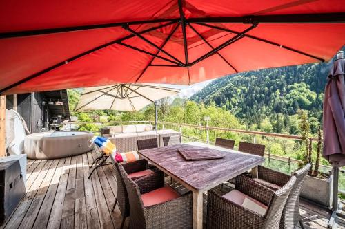 a table and chairs on a deck with a red umbrella at Chalet Elisthur in Saint-Jean-dʼAulps