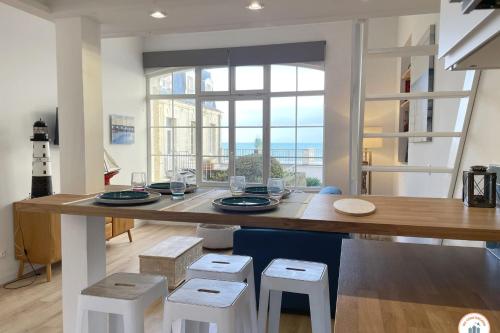 une cuisine avec une grande table en bois avec des tabourets blancs dans l'établissement Le Sunset - Vue Mer - Accès plage privé, à Trouville-sur-Mer