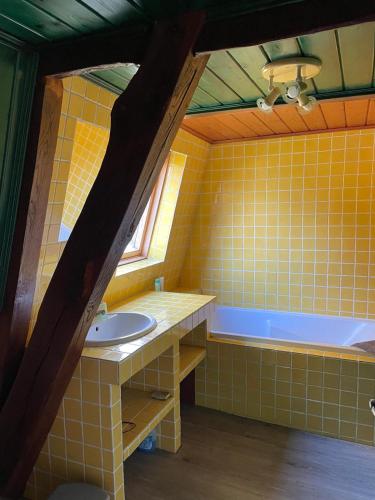La salle de bains est pourvue de carrelage jaune, d'un lavabo et d'une baignoire. dans l'établissement La Caminade, à Bourg-de-Bigorre