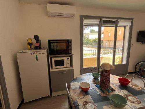 La cuisine est équipée d'une table, d'un four micro-ondes et d'un réfrigérateur. dans l'établissement Appartement Beau Rivage Narbonne Plage, à Narbonne-Plage