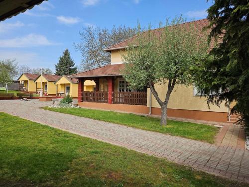 a house with a tree next to a brick sidewalk at Estike Apartmanok in Tiszafüred