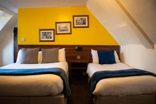 two beds in a room with a yellow wall at Scole Inn Hotel in Diss