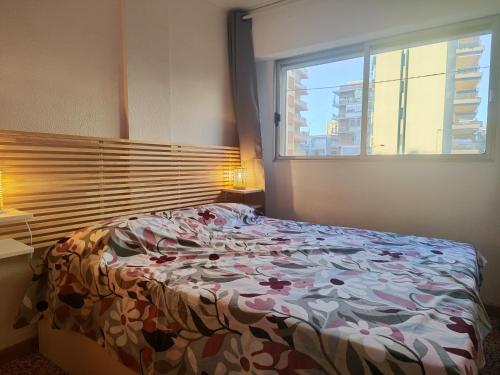 a bedroom with a bed with a floral comforter and a window at Gran piso cerca del mar in Puerto de Gandía