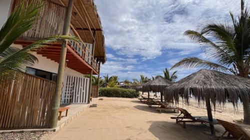 a row of chairs and straw umbrellas on a beach at Baja Canoas Hotel in Canoas De Punta Sal