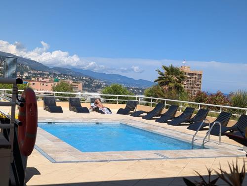 une femme assise sur des chaises longues à côté d'une piscine dans l'établissement Studio Apart Monaco Palais, à Rocquencourt