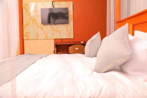 a white bed with pillows and a television on a wall at Country Sights Hotel, BULISA in Bulisa